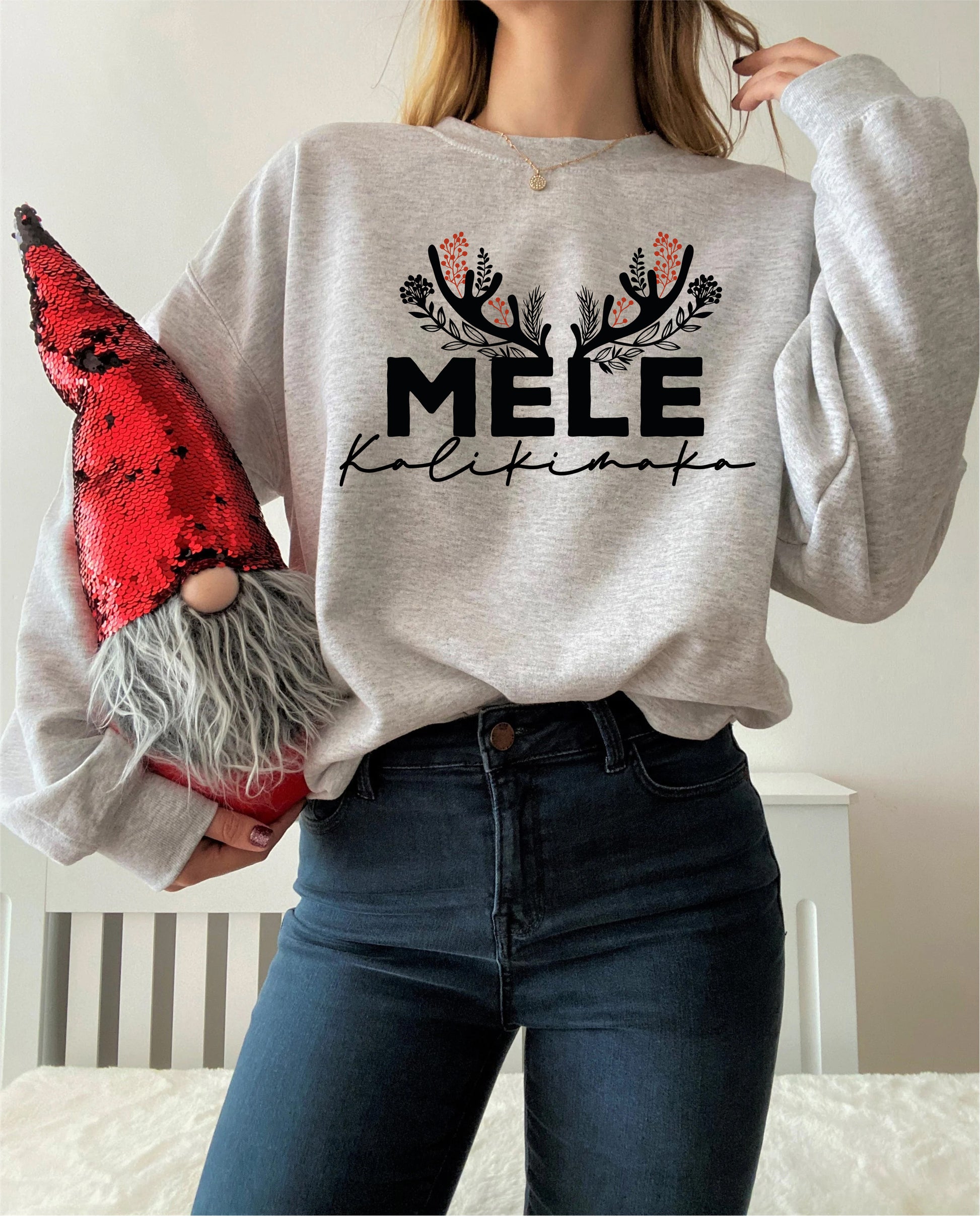 A woman wearing a grey sweatshirt with a graphic design and holding a red sequined gnome.