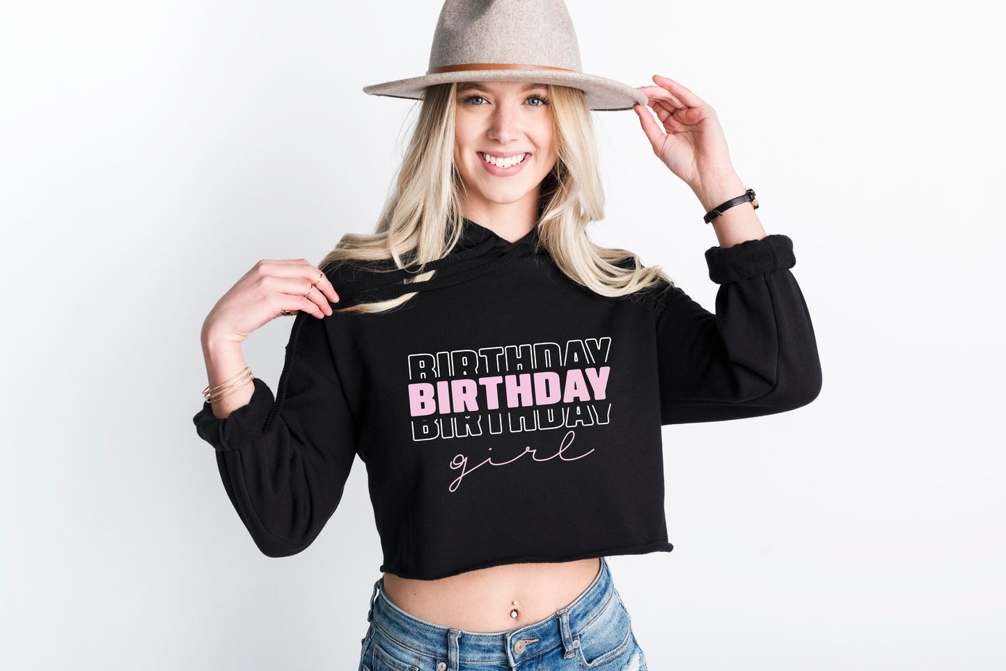 A smiling woman wearing a black hoodie with the text "BIRTHDAY BIRTHDAY GIRL" printed on it, along with a gray hat.