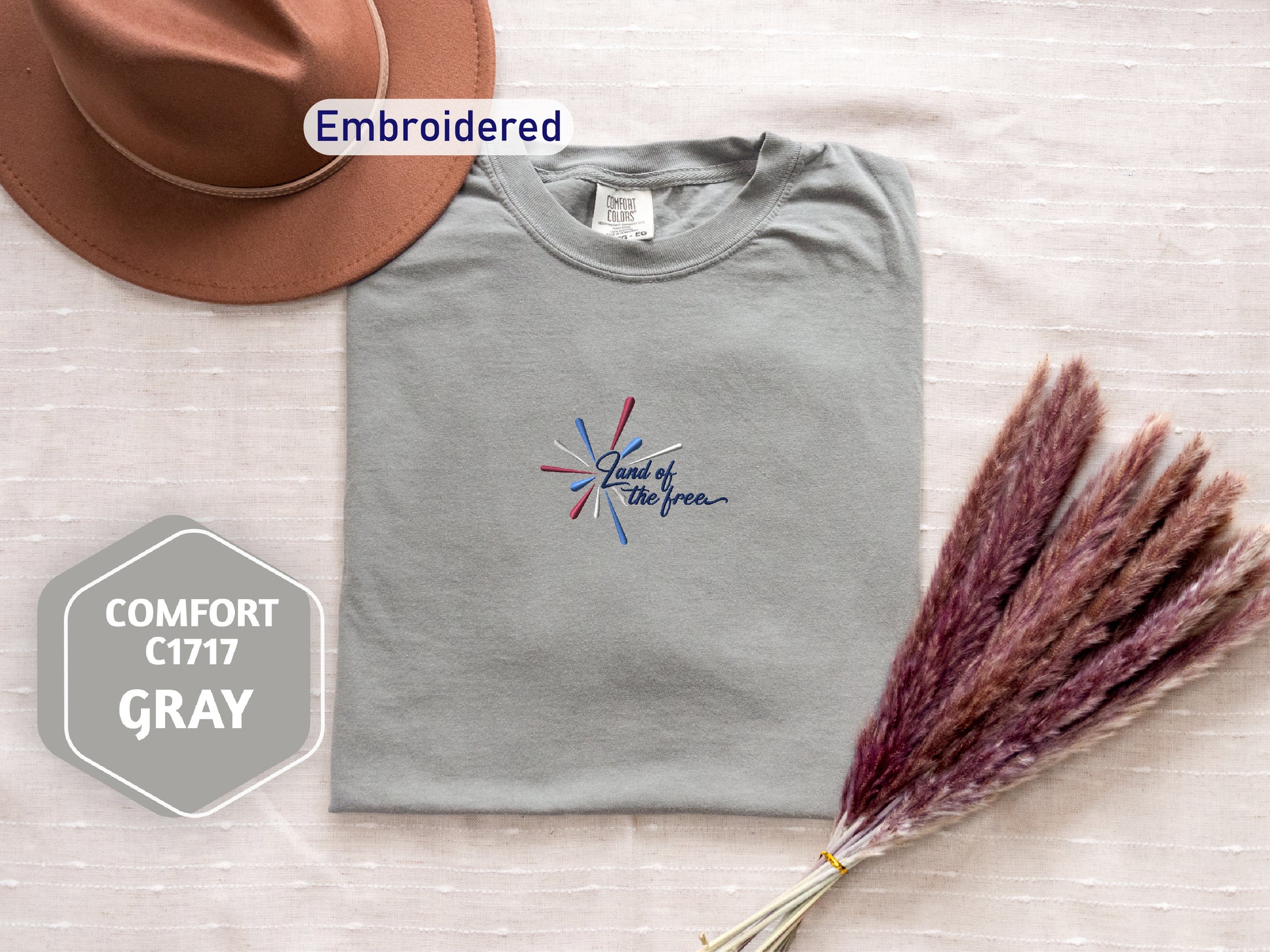 a gray t-shirt with a patriotic design, a brown hat, and a bunch of purple and red pom poms, all arranged on a white background.