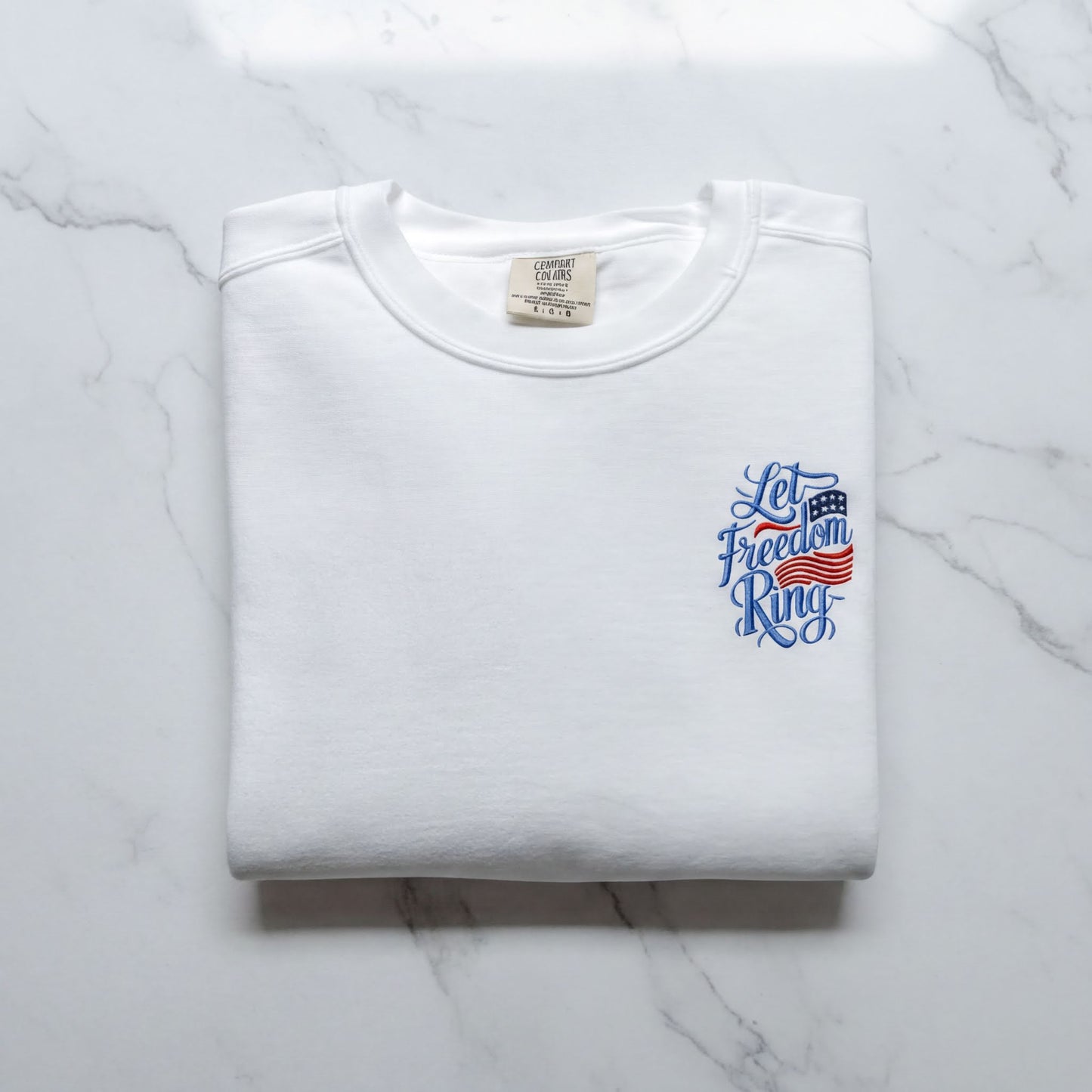 A white t-shirt with a blue and red design on the left side, featuring the text "Let Freedom Ring" in a stylized font.