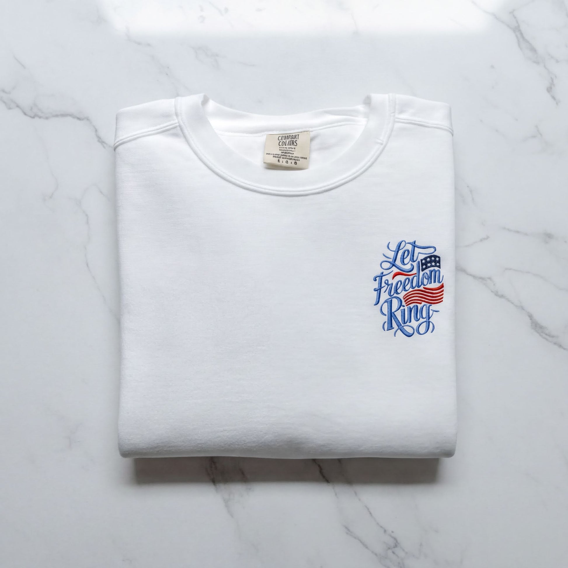 A white t-shirt with a blue and red design on the left side, featuring the text "Let Freedom Ring" in a stylized font.