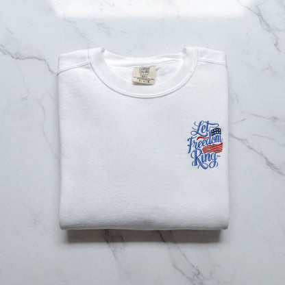 A white t-shirt with a blue and red design on the left side, featuring the text "Let Freedom Ring" in a stylized font.