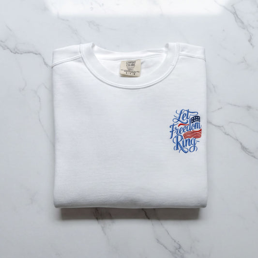 A white t-shirt with a blue and red design on the left side, featuring the text "Let Freedom Ring" in a stylized font.