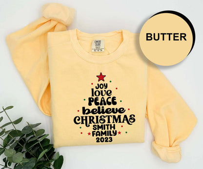 A yellow t-shirt with a Christmas tree design and text printed on it, along with a label and a circular logo with the word "BUTTER" on it.