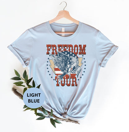 A light blue t-shirt with a graphic design featuring an eagle and the text "FREEDOM TOUR" printed on it.