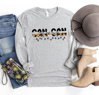 A casual outfit consisting of a gray long-sleeved t-shirt with a graphic design, a pair of blue jeans, a gray hat, and beige ankle boots, along with a floral-patterned purse and a pair of sunglasses.