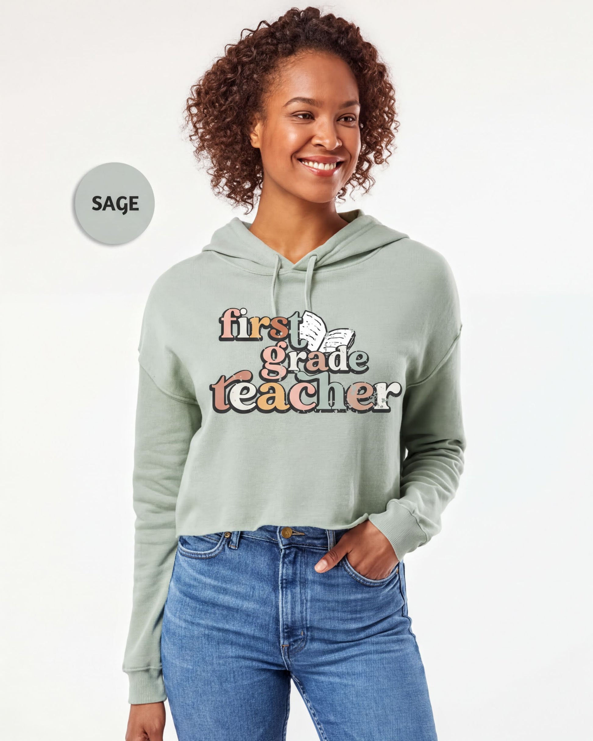 A smiling woman wearing a light green hoodie with text that says "first grade teacher" printed on it.