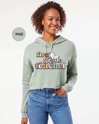 A smiling woman wearing a light green hoodie with text that says "first grade teacher" printed on it.