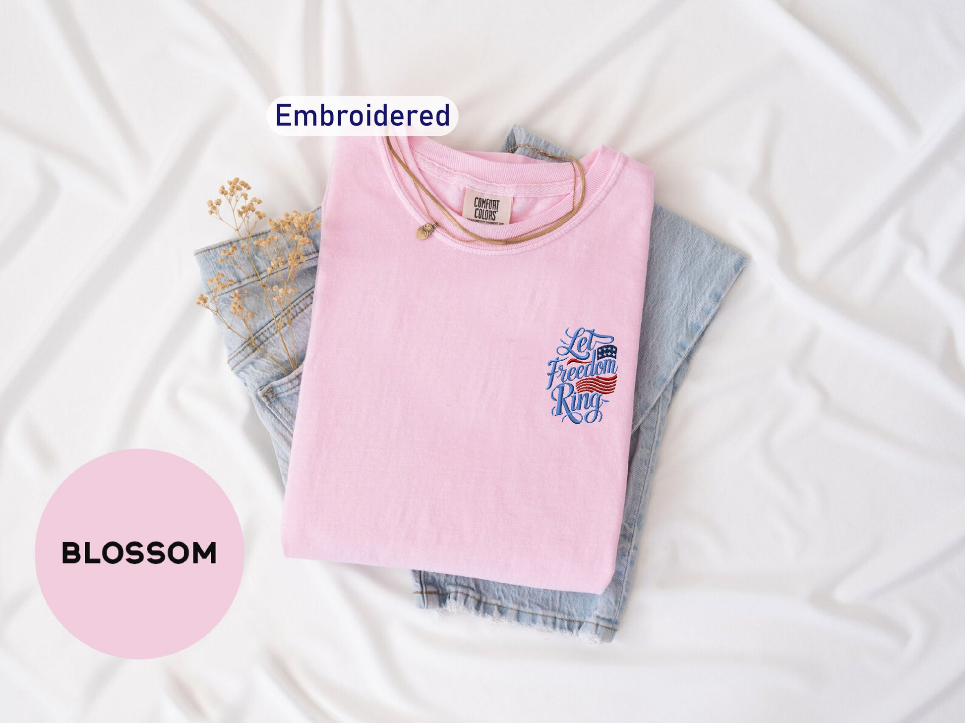 a pink t-shirt with a graphic design, a pair of denim jeans, and some dried flowers, all laid out on a white background.
