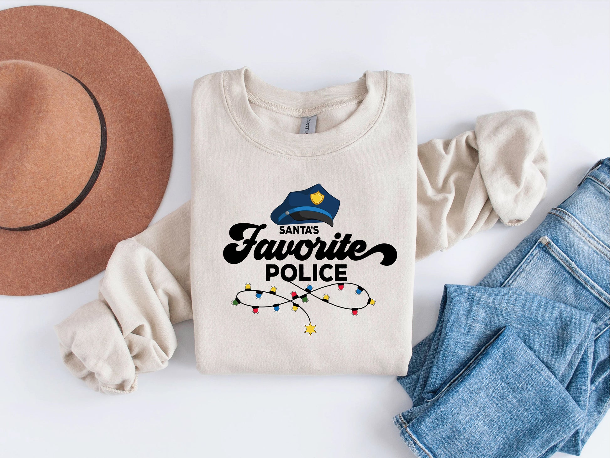 A white sweatshirt with a graphic design and text, a brown hat, and a pair of blue jeans are arranged on a white background.