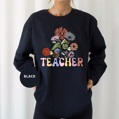 a woman wearing a black teacher sweatshirt with flowers on it