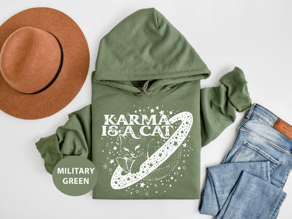 a green hoodie with the words karma is a cat on it next to a