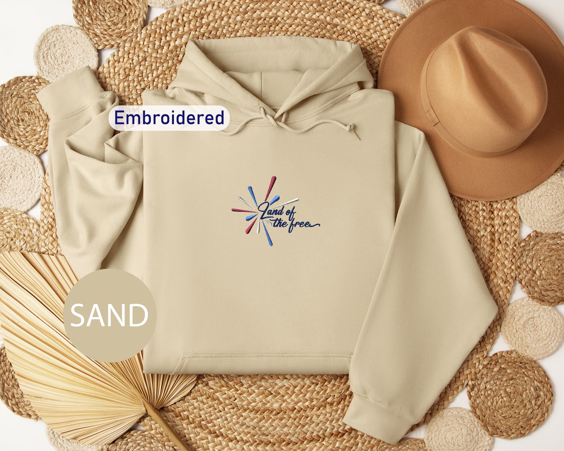 a beige hoodie with a colorful design, a brown hat, and a straw hat, all arranged on a woven mat.