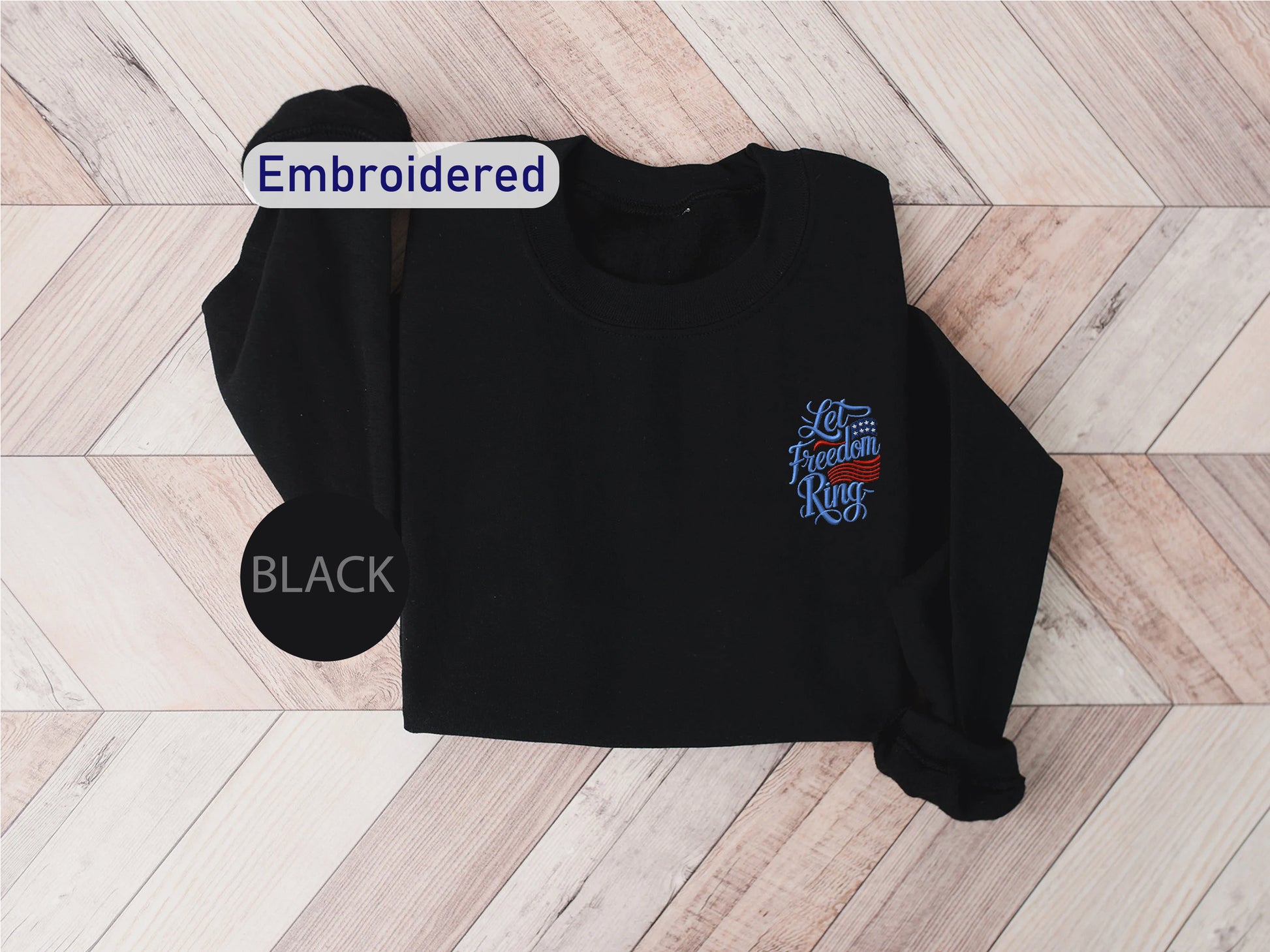 A black sweater with a blue embroidered design on the front, laid out on a wooden surface.