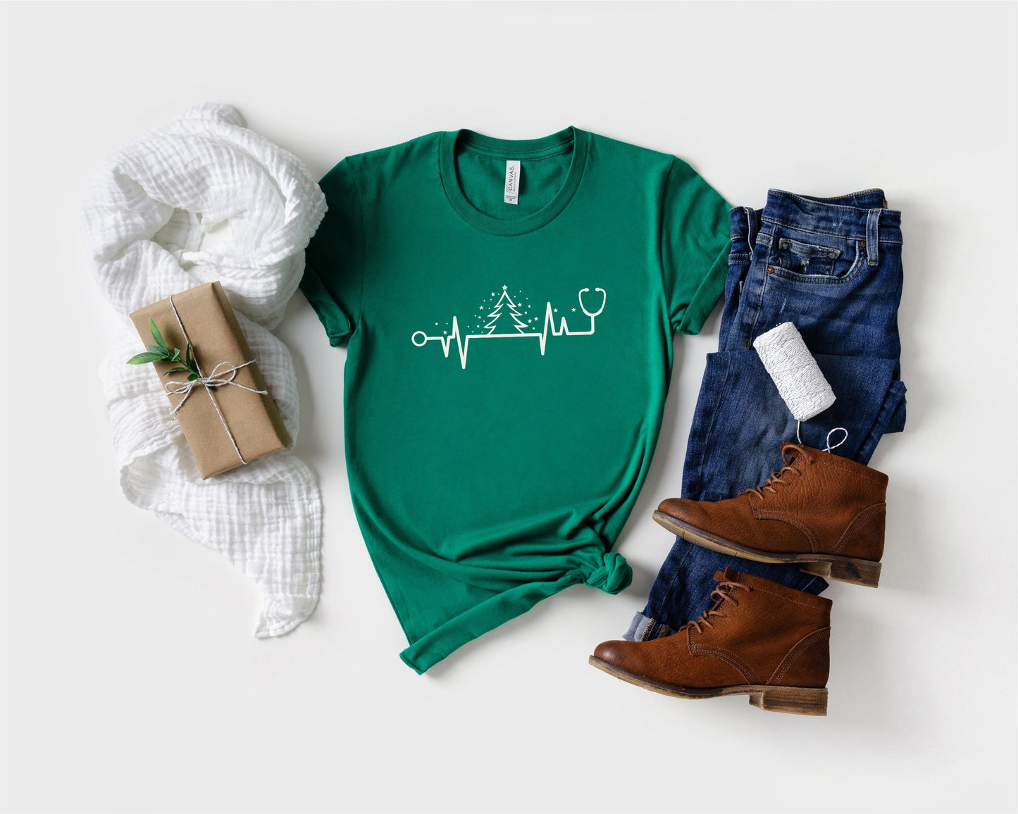 A green t-shirt with a white line drawing of a stethoscope and a tree, a pair of blue jeans, brown boots, and a wrapped gift box.
