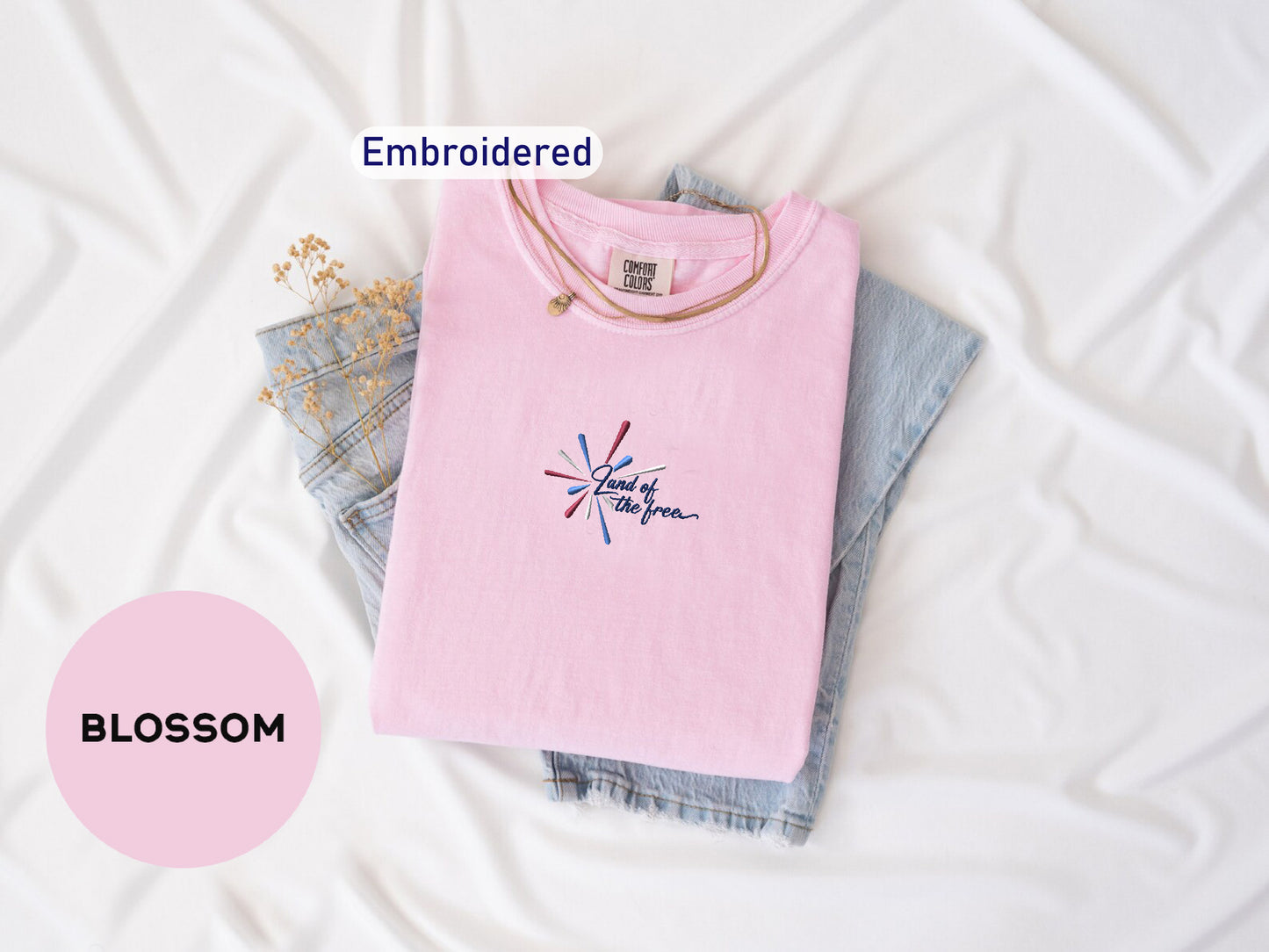 a pink t-shirt with a graphic design, a pair of blue jeans, and some dried flowers, all laid out on a white background.