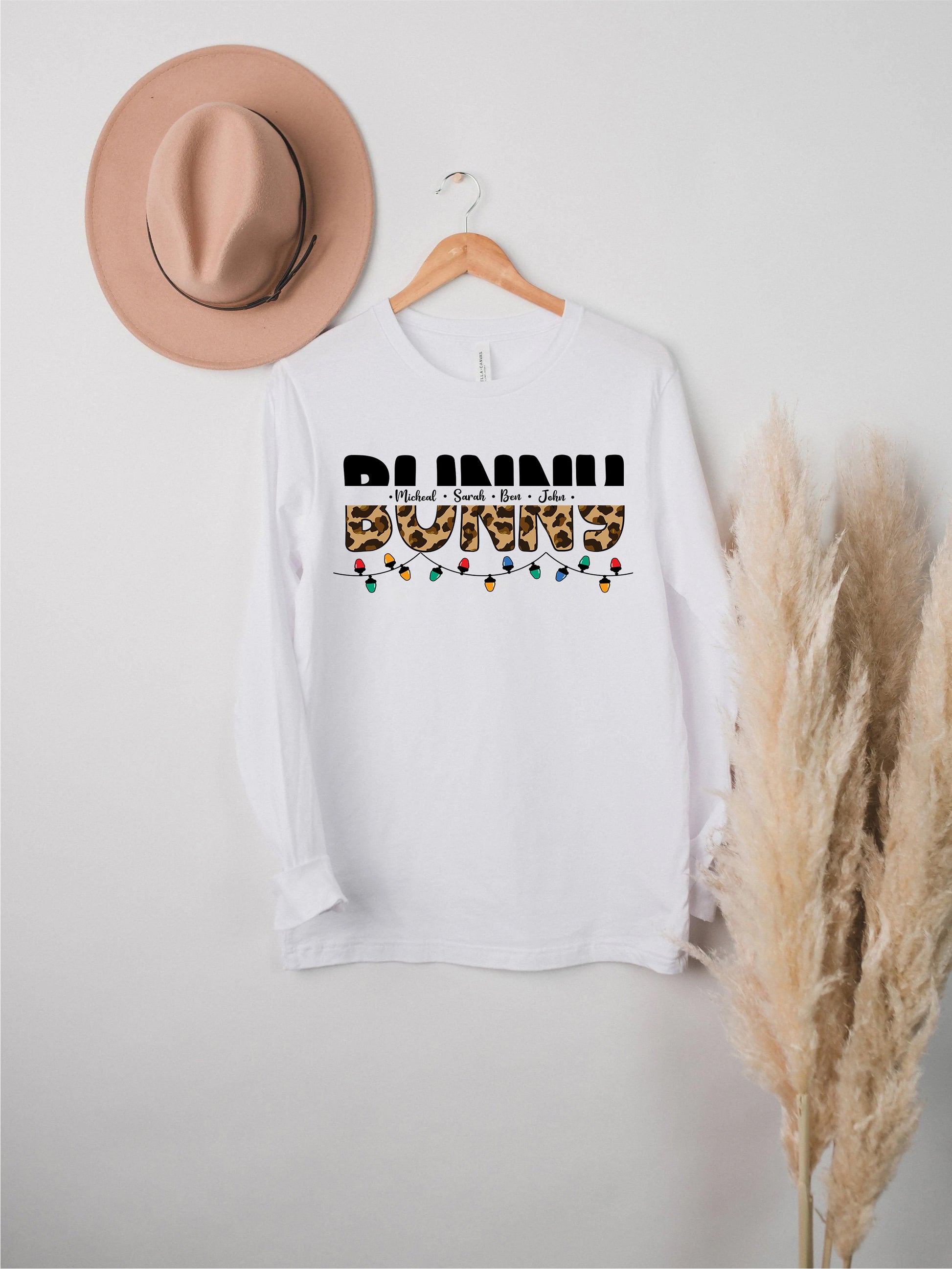 A white long-sleeved t-shirt with the text "BUNNI" printed on it, along with a beige hat and some potted plants in the background.