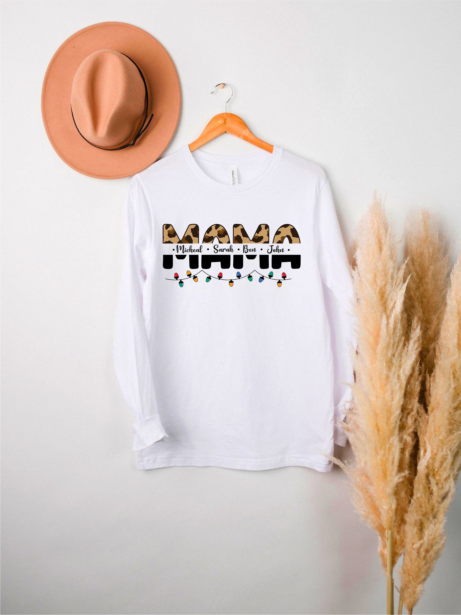 A white long-sleeved t-shirt with the text "Mama" printed on it, along with a brown hat and some potted plants in the background.