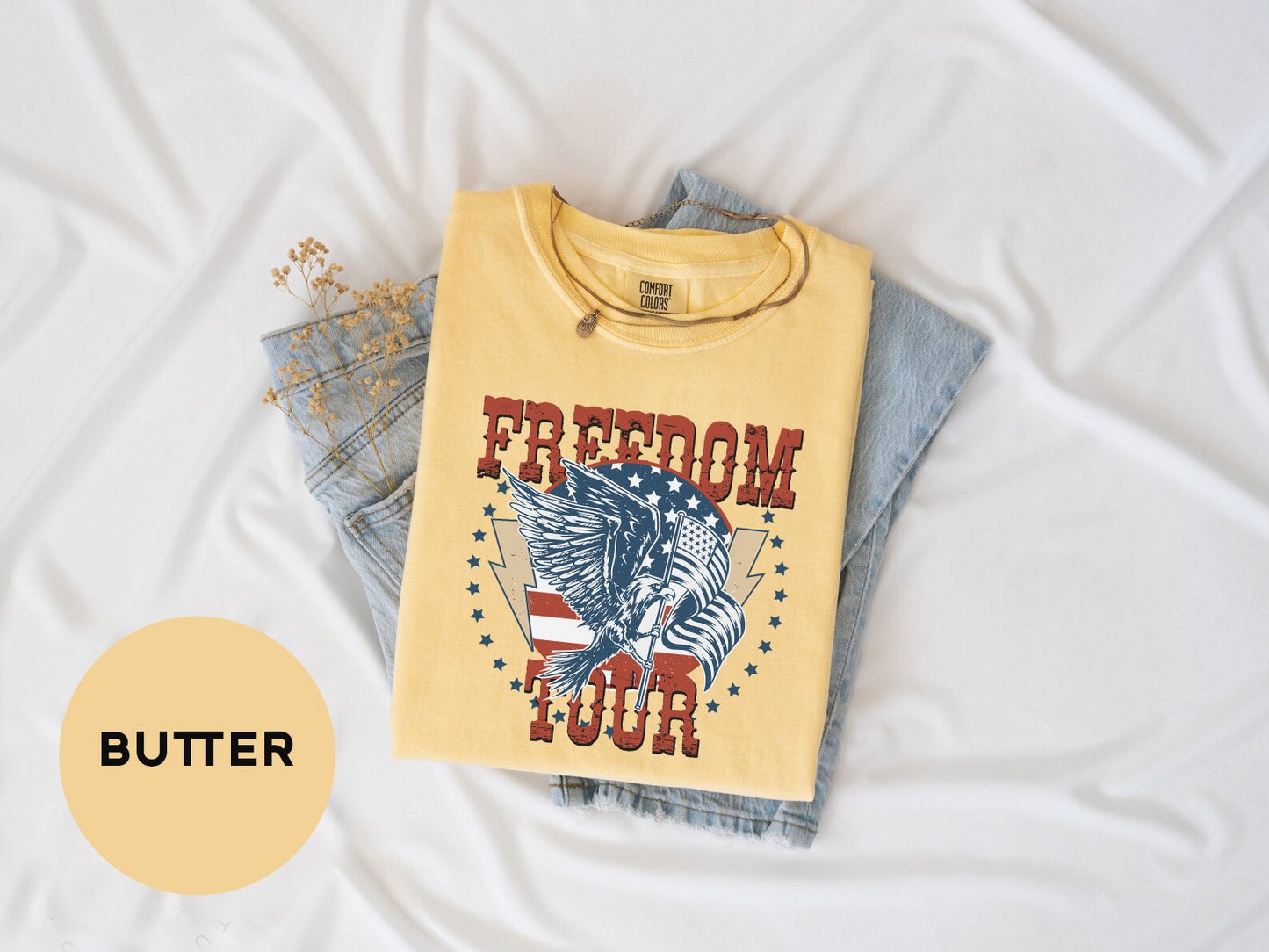 a yellow t-shirt with a graphic design, a pair of blue jeans, and some dried flowers on a white background.