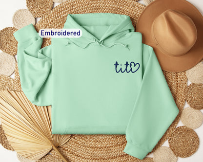 a green hoodie with embroidered tic2 on it next to a straw hat