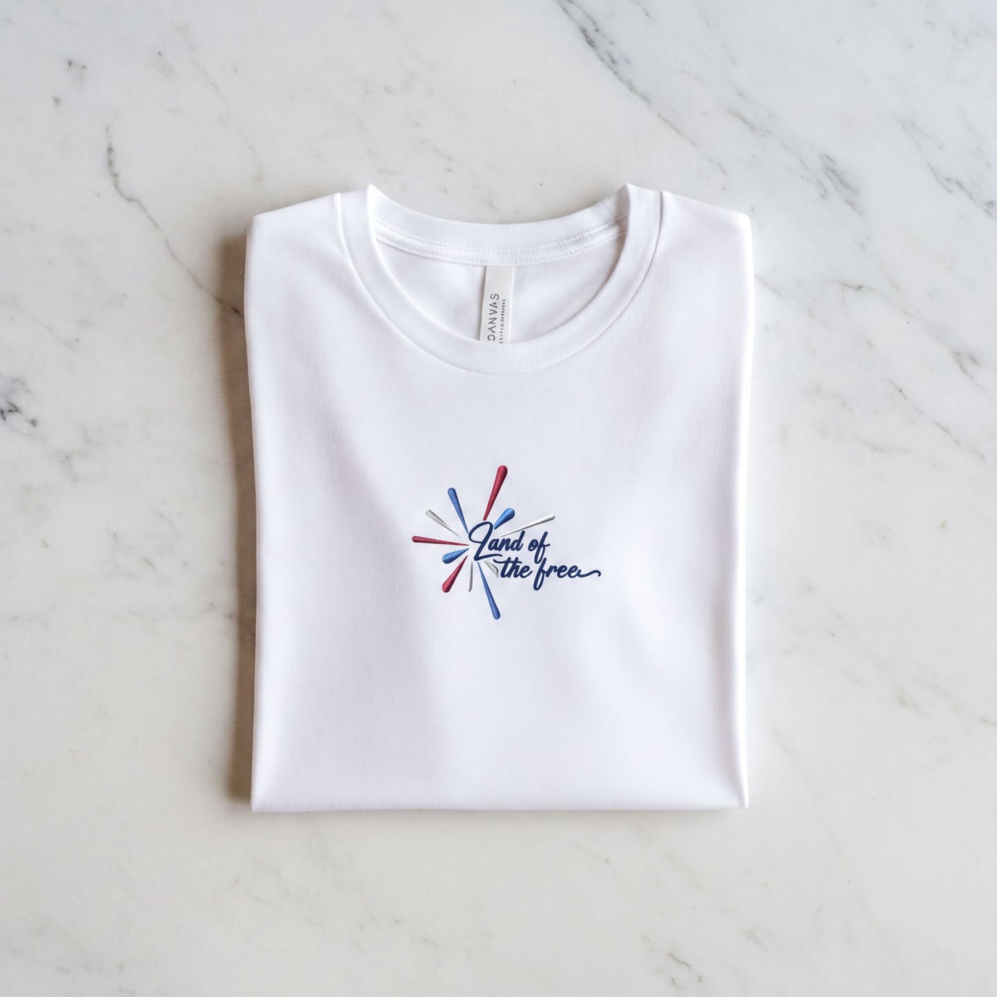 A white t-shirt with a graphic design and text printed on it, laid out on a marble surface.