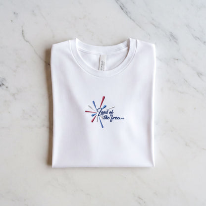 A white t-shirt with a graphic design and text printed on it, laid out on a marble surface.