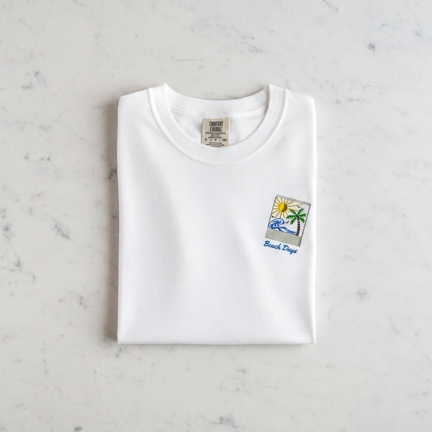 A white t-shirt with a small graphic design and text printed on it, laid out on a marble surface.