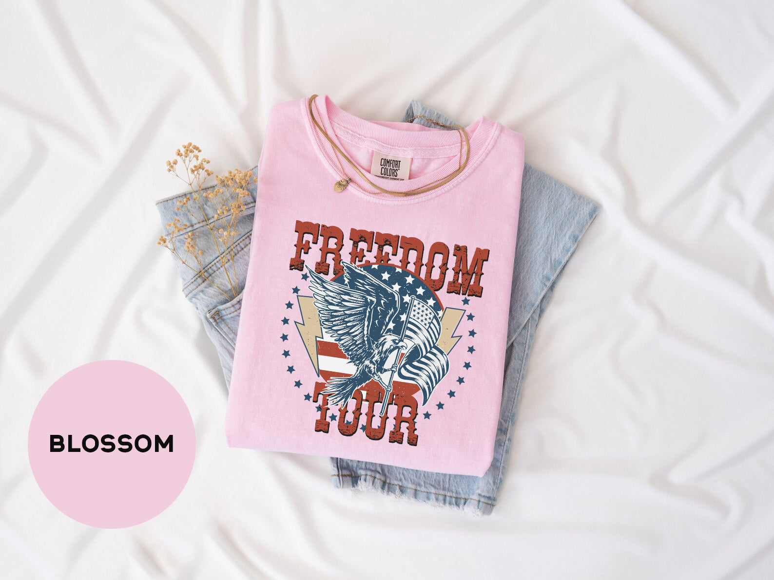 A pink t-shirt with the text "FREEDOM FOUR" printed on it, along with an image of an eagle and an American flag, is laid out on a white surface.