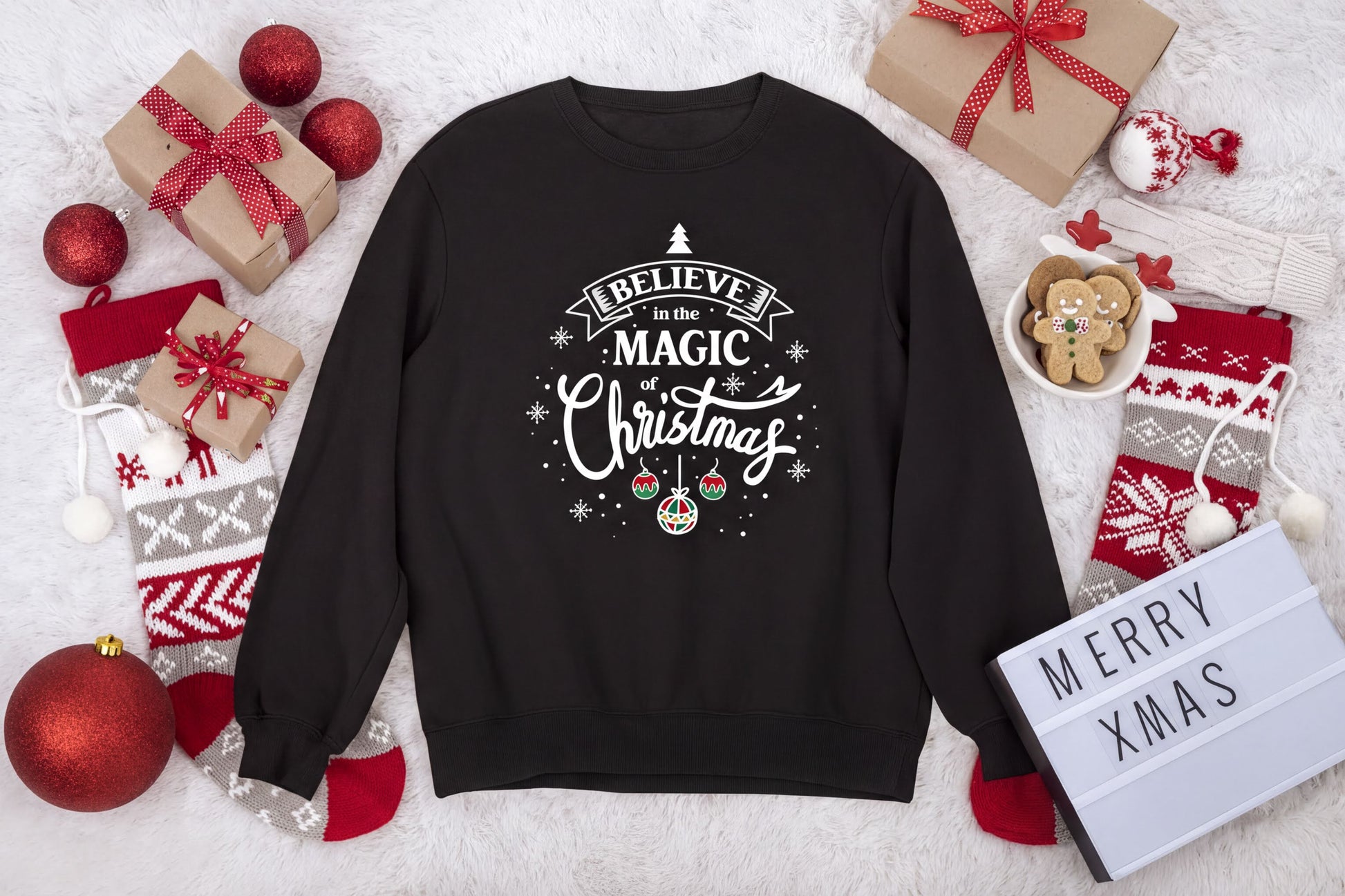 A black sweatshirt with a Christmas-themed design, surrounded by various holiday decorations and gifts, including a sign that says "Merry Xmas".