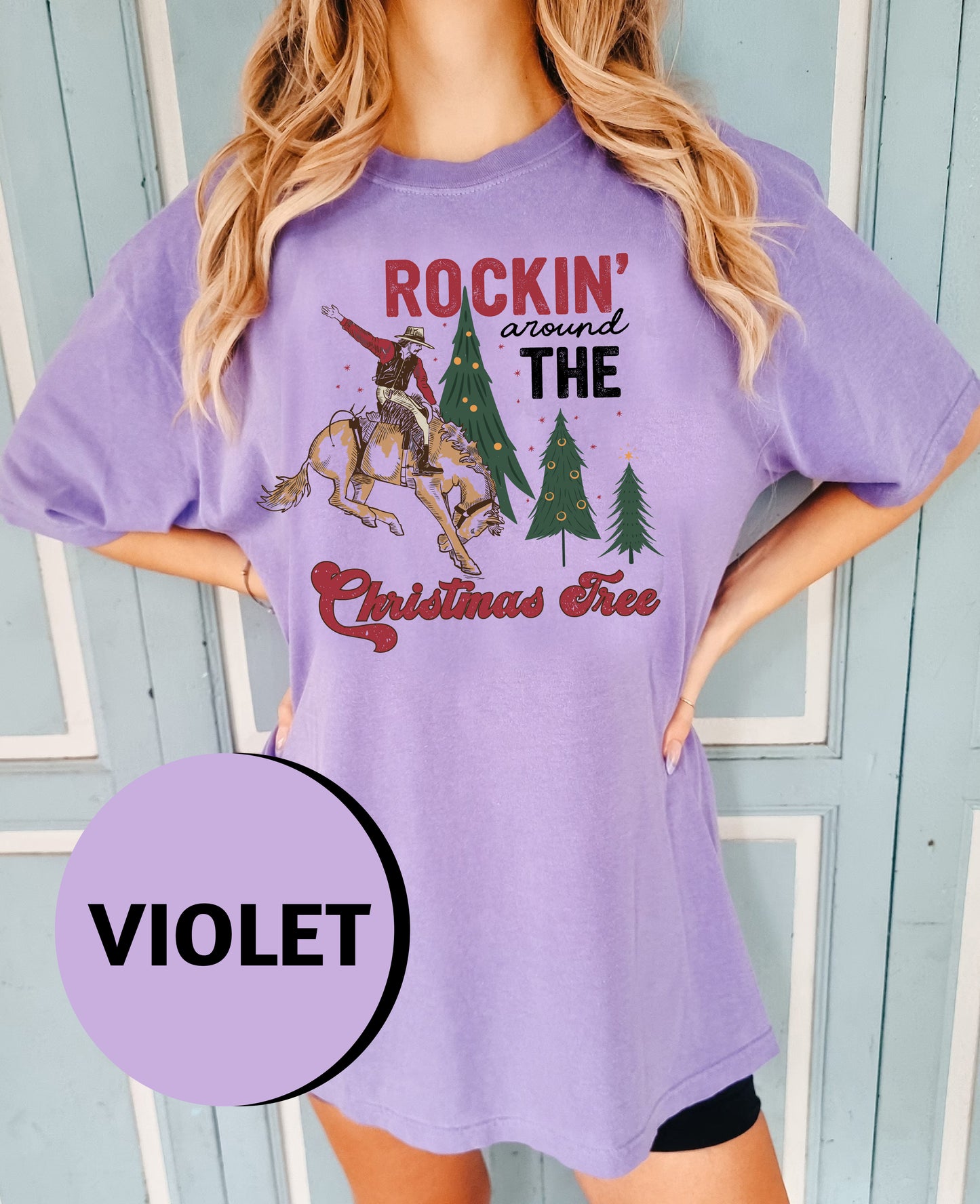 A woman wearing a purple t-shirt with a graphic design of a cowboy on a horse and Christmas trees.