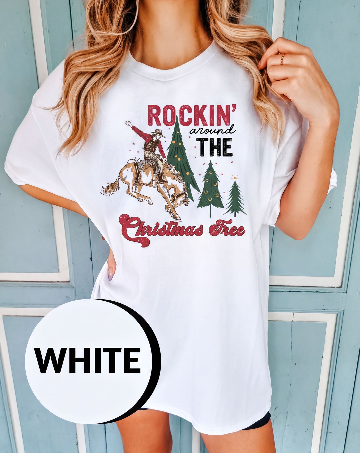 A woman wearing a white t-shirt with a graphic design of a cowboy riding a bucking bronco, along with Christmas trees and the text "ROCKIN' around THE CHRISTMAS FREE".