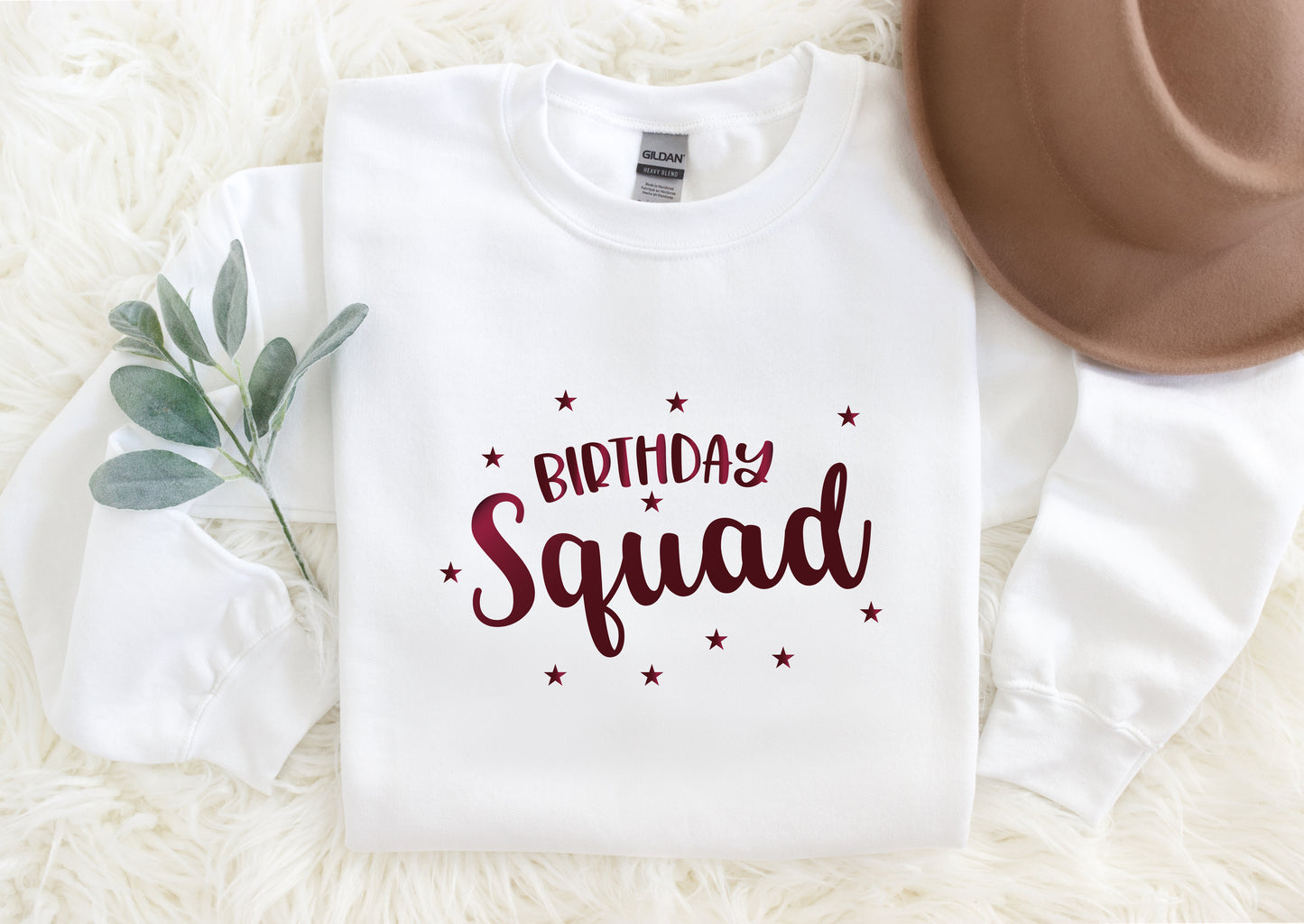 A white t-shirt with a red text design that says "Birthday Squad" surrounded by stars, placed on a white fur rug.