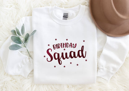 A white t-shirt with a red text design that says "Birthday Squad" surrounded by stars, placed on a white fur rug.
