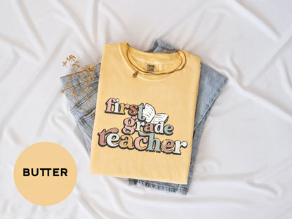 A yellow t-shirt with the text "first grade teacher" printed on it, along with a denim skirt, laid out on a white surface.