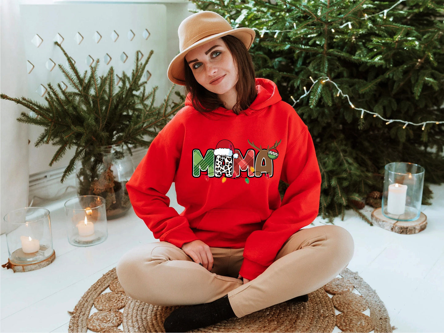 A woman wearing a red hoodie with the word "MOMA" on it, sitting on a rug in front of a Christmas tree.