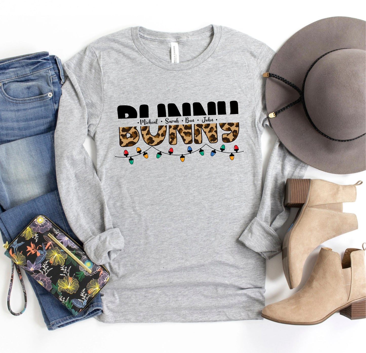 A casual outfit consisting of a gray long-sleeved t-shirt with a leopard print design, a pair of blue jeans, a gray hat, and beige ankle boots, along with a floral-patterned purse and a pair of sunglasses.
