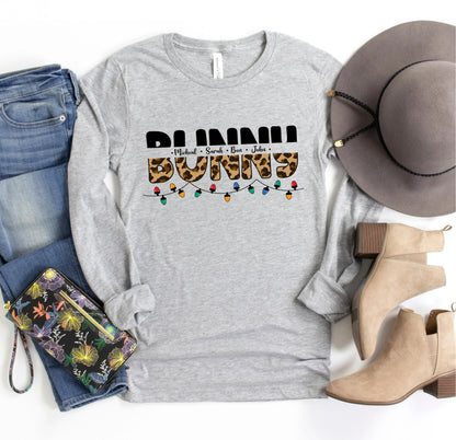 A casual outfit consisting of a gray long-sleeved t-shirt with a leopard print design, a pair of blue jeans, a gray hat, and beige ankle boots, along with a floral-patterned purse and a pair of sunglasses.