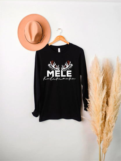 A black long-sleeved shirt with white text and decorative antlers is hanging on a wooden hanger against a white wall.