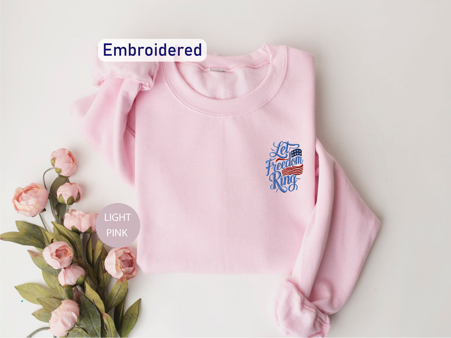 A pink sweatshirt with an embroidered design and the text "Let's fight the war" is displayed alongside a bouquet of pink flowers.