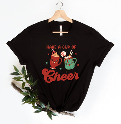 A black t-shirt with a graphic design featuring two colorful mugs and the text "Have a Cup of Cheer" along with a star symbol.