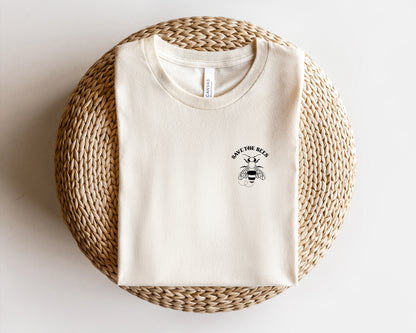A white t-shirt with a graphic of a bee and the text "SAVE THE BEES" printed on it, laid out on a woven basket.