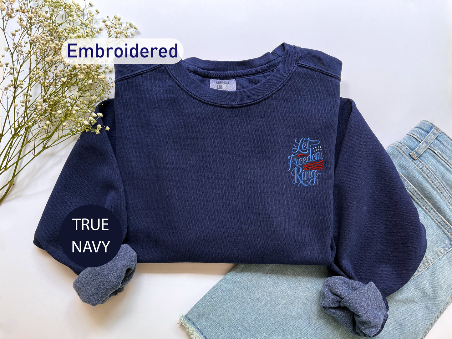 a navy blue sweater with an embroidered design, a pair of blue jeans, and a pair of blue socks, all laid out on a white surface.