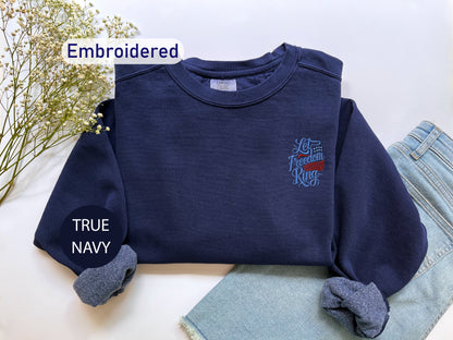a navy blue sweater with an embroidered design, a pair of blue jeans, and a pair of blue socks, all laid out on a white surface.