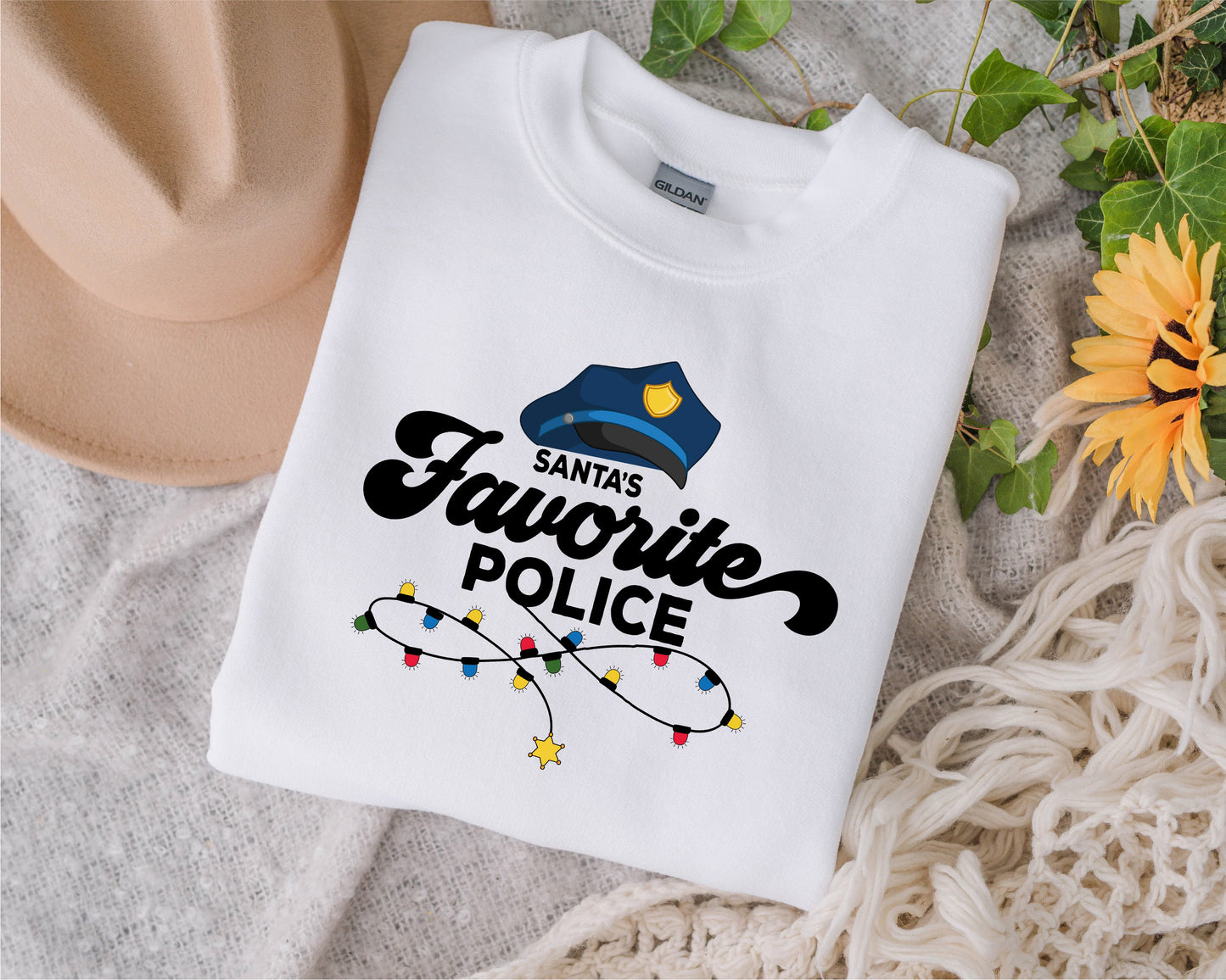 A white t-shirt with a graphic design and text, along with a hat and some greenery, is displayed on a surface.