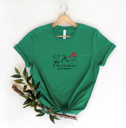 A green t-shirt with a Christmas-themed graphic design, including a small illustration of a dog wearing a Santa hat, is hanging on a wooden hanger.