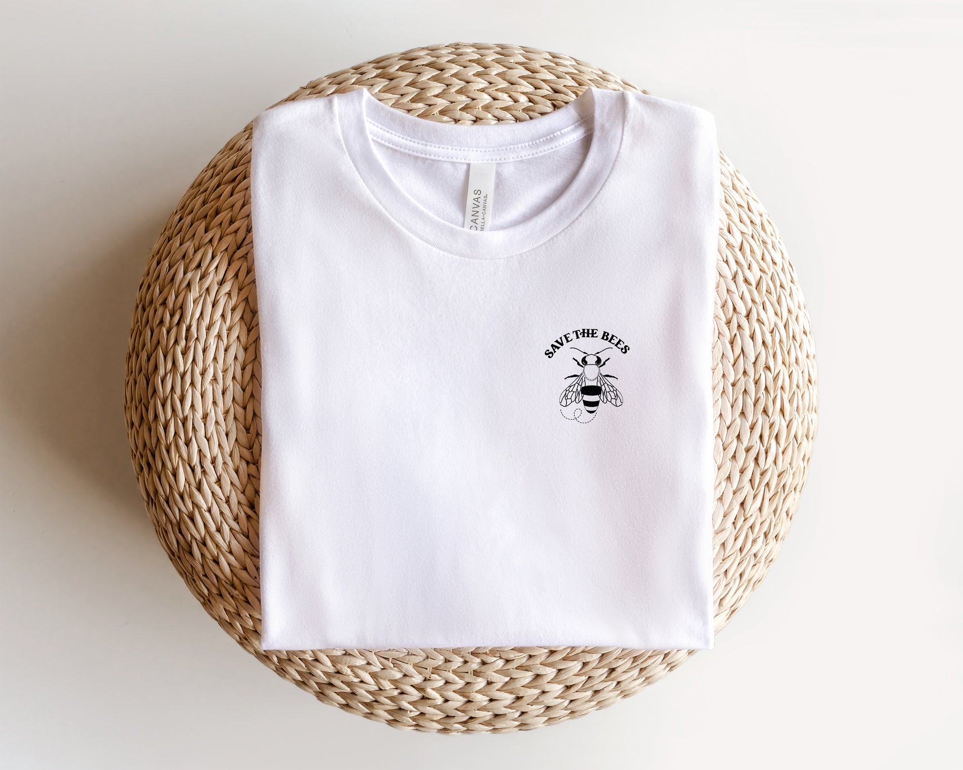 A white t-shirt with a graphic design and text printed on it, placed on a woven basket or mat.