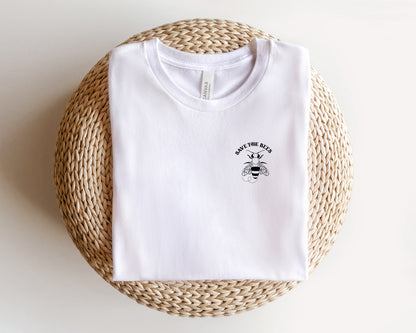 A white t-shirt with a graphic design and text printed on it, placed on a woven basket or mat.