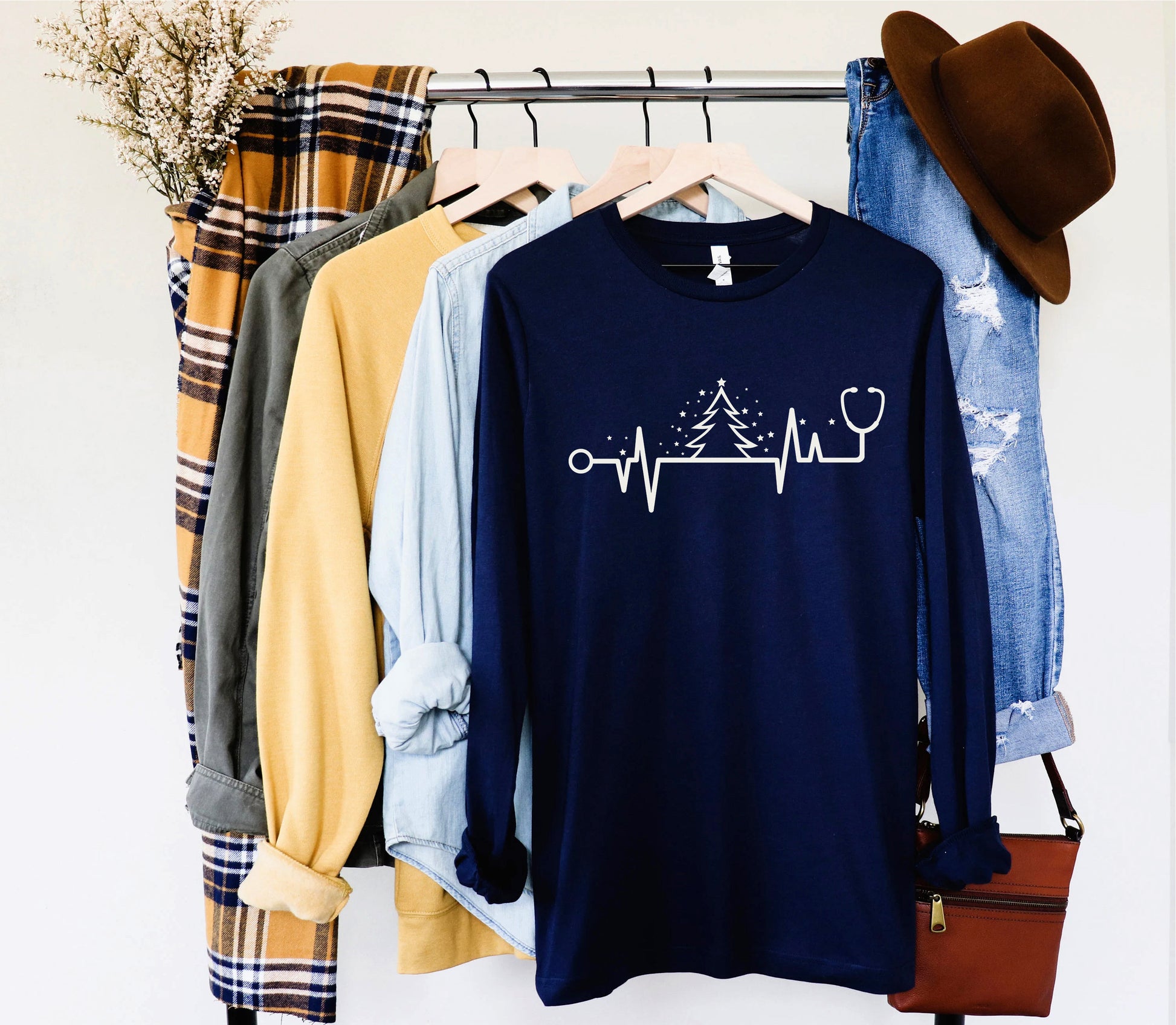 A clothing rack displaying various items, including a blue long-sleeve shirt with a white line design, a plaid shirt, a yellow shirt, and a pair of blue jeans.