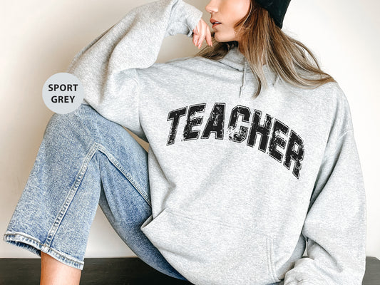 a woman sitting on the ground wearing a sweatshirt with the word teacher on it