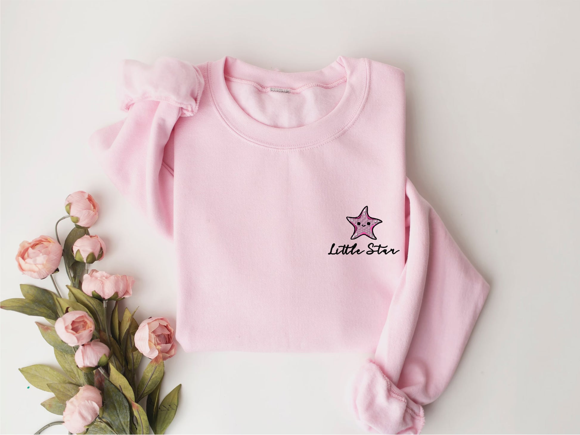 a pink sweater with a star on it next to flowers